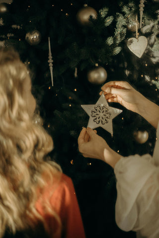 Two people decorating a Christmas tree with star-shaped ornaments.